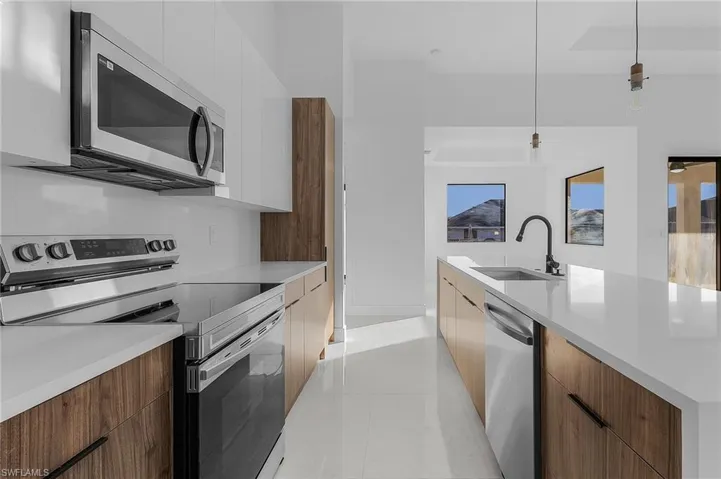 Kitchen with stainless steel appliances, modern cabinets, pendant lighting, light stone counters, and light tile patterned flooring