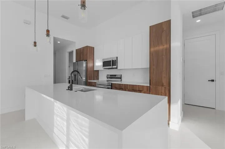 Kitchen with white cabinets, modern cabinets, stainless steel appliances, brown cabinets, and pendant lighting