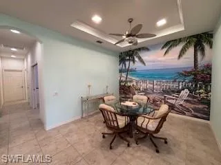 Dining space featuring a ceiling fan, arched walkways, baseboards, a tray ceiling, and recessed lighting