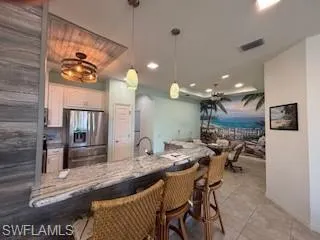 Kitchen featuring light tile patterned flooring, a kitchen breakfast bar, white cabinets, stainless steel fridge with ice dispenser, and hanging light fixtures