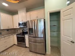 Kitchen featuring backsplash, light stone countertops, light tile patterned floors, white cabinets, and stainless steel appliances