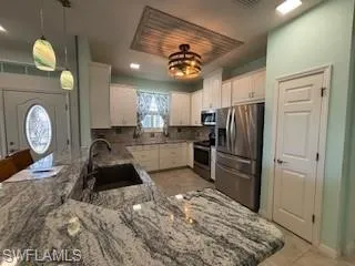 Kitchen featuring appliances with stainless steel finishes, light stone countertops, a sink, a peninsula, and white cabinetry