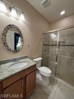 Bathroom featuring vanity, toilet, visible vents, and a stall shower