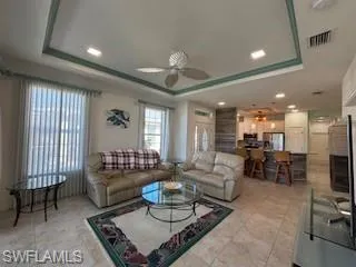 Living area with light tile patterned flooring, ceiling fan, a raised ceiling, recessed lighting, and visible vents