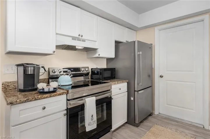 Kitchen featuring light hardwood / wood-style flooring, white cabinets, dark stone countertops, and appliances with stainless steel finishes