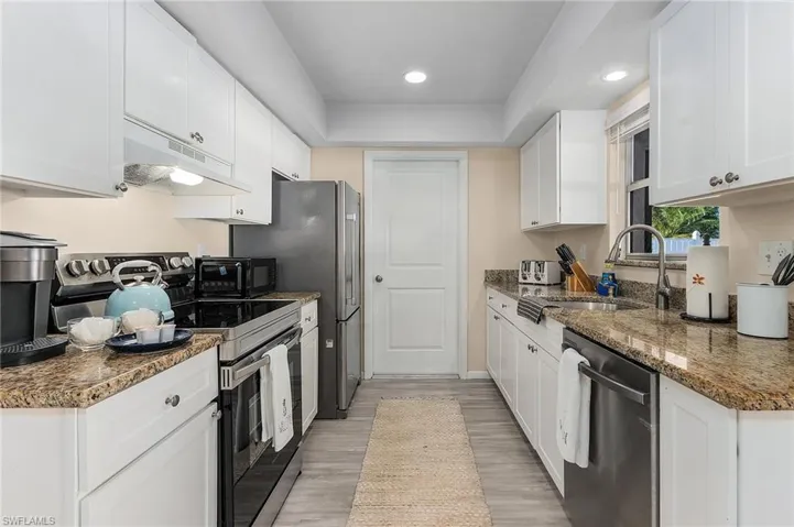 Kitchen with dark stone countertops, white cabinetry, stainless steel appliances, light hardwood / wood-style flooring, and sink