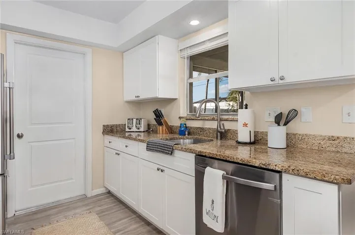 Kitchen with dark stone countertops, white cabinets, light wood-type flooring, stainless steel dishwasher, and sink