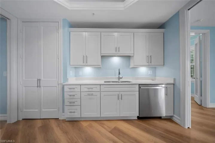 Kitchen with ornamental molding, sink, light hardwood / wood-style floors, white cabinets, and stainless steel dishwasher