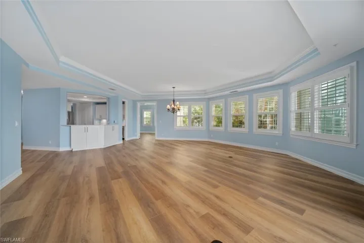 Unfurnished living room with light hardwood / wood-style floors, a notable chandelier, crown molding, and a tray ceiling