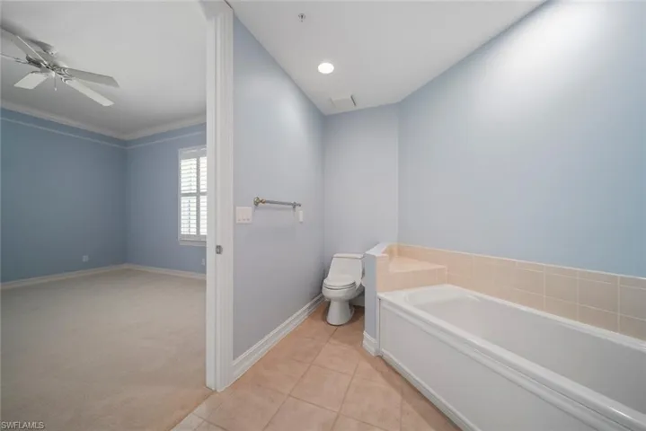 Bathroom featuring tile patterned flooring, ornamental molding, ceiling fan, a washtub, and toilet