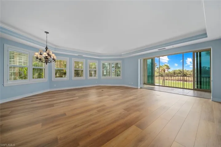Empty room with a notable chandelier, a raised ceiling, crown molding, and light hardwood / wood-style flooring