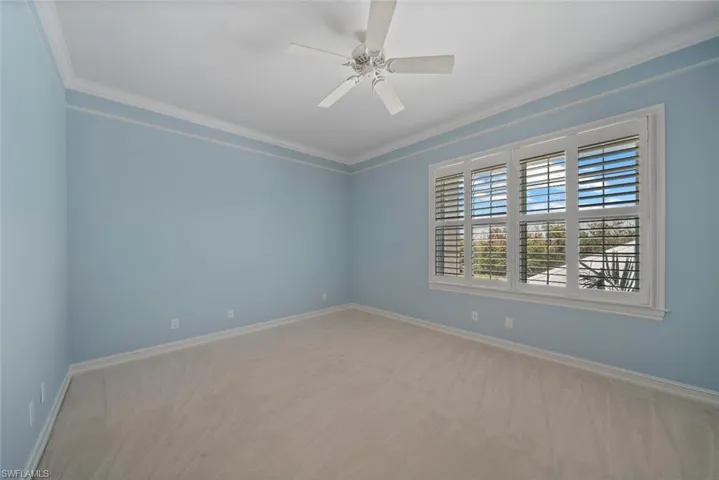 Carpeted empty room featuring ceiling fan and crown molding