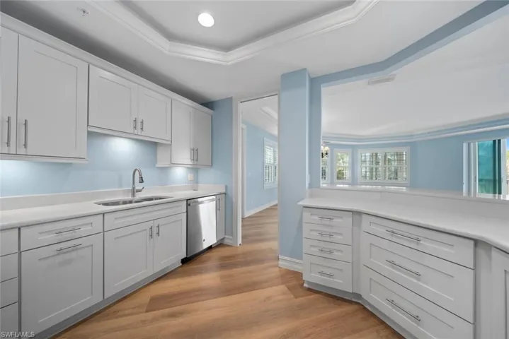 Kitchen featuring light wood-type flooring, stainless steel dishwasher, sink, and a tray ceiling