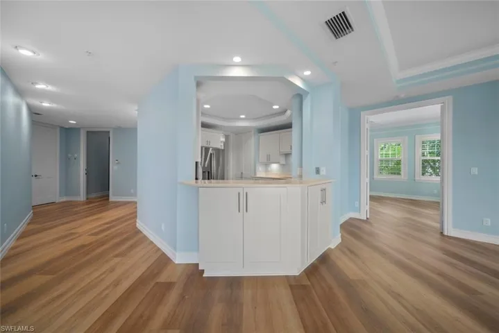 Kitchen featuring kitchen peninsula, ornamental molding, hardwood / wood-style floors, white cabinets, and stainless steel fridge