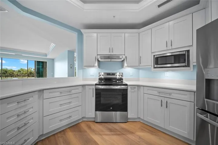 Kitchen with stainless steel appliances, white cabinets, crown molding, a raised ceiling, and light hardwood / wood-style flooring
