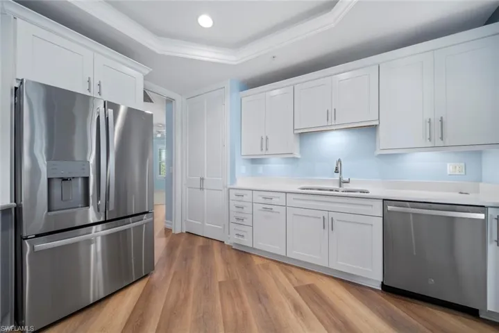 Kitchen with white cabinetry, stainless steel appliances, light hardwood / wood-style floors, and a tray ceiling