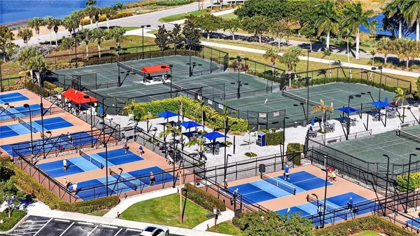 Recreational complex featuring multiple fenced tennis courts and pickleball courts with paved surfaces and overhead lighting
