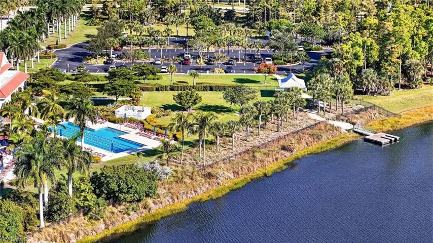 Aerial perspective featuring a waterfront lap pool, expansive green space, mature palm trees, paved parking, and a private dock