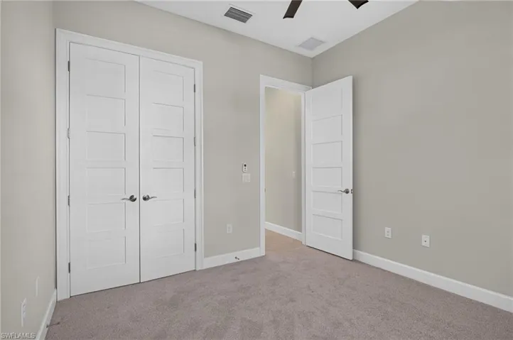 Neutral-toned interior room featuring carpeted flooring, five-panel interior doors, and a ceiling-mounted fan