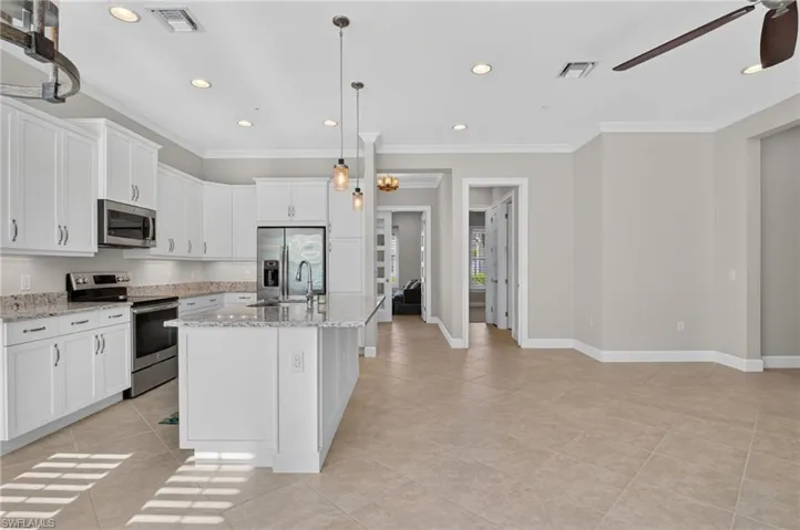 Kitchen featuring white cabinetry, stone-finish countertops, stainless steel appliances, a central island with pendant lighting, and neutral tile flooring