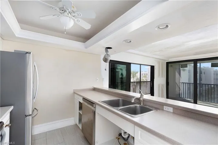 Kitchen with ceiling fan, sink, white cabinetry, a tray ceiling, and appliances with stainless steel finishes