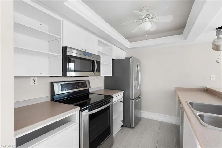Kitchen featuring sink, white cabinets, a raised ceiling, appliances with stainless steel finishes, and ceiling fan