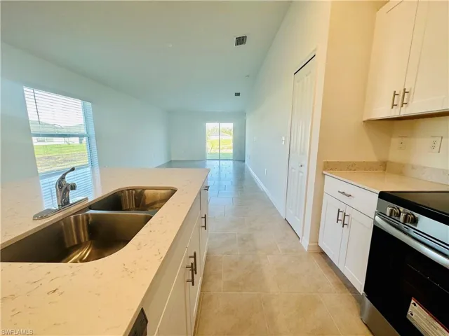 Kitchen featuring white cabinets, stainless steel electric range, light stone countertops, lofted ceiling, and light tile patterned floors