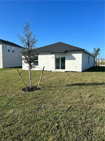 Back of property with a yard, stucco siding, and roof with shingles