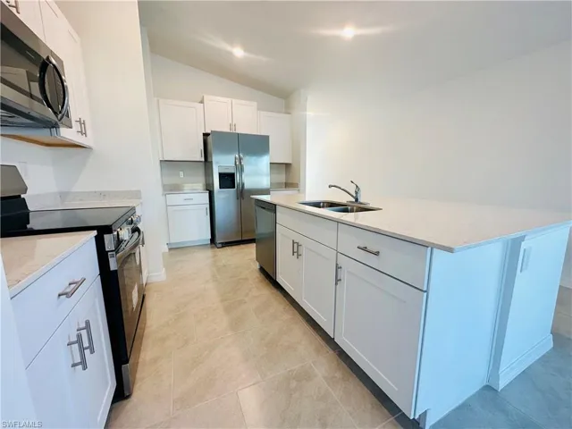 Kitchen with appliances with stainless steel finishes, lofted ceiling, light stone countertops, white cabinetry, and a center island with sink