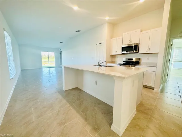 Kitchen with white cabinetry, stainless steel appliances, a center island with sink, lofted ceiling, and open floor plan