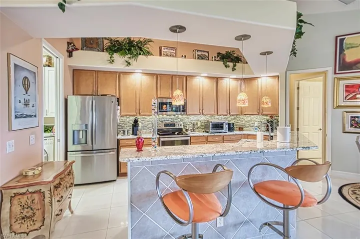 Kitchen featuring a breakfast bar area, light tile patterned flooring, appliances with stainless steel finishes, and decorative backsplash