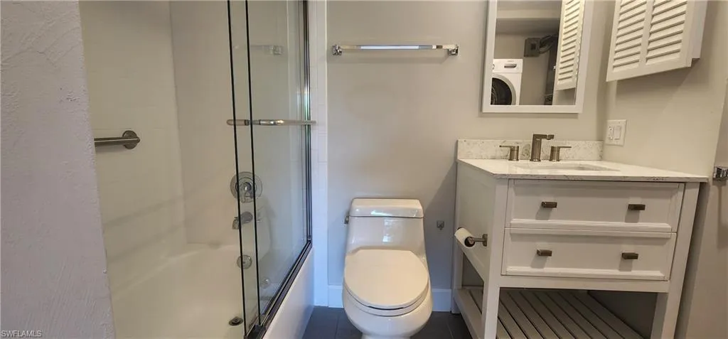 Full bathroom featuring washer / dryer, toilet, tile flooring, bath / shower combo with glass door, and vanity