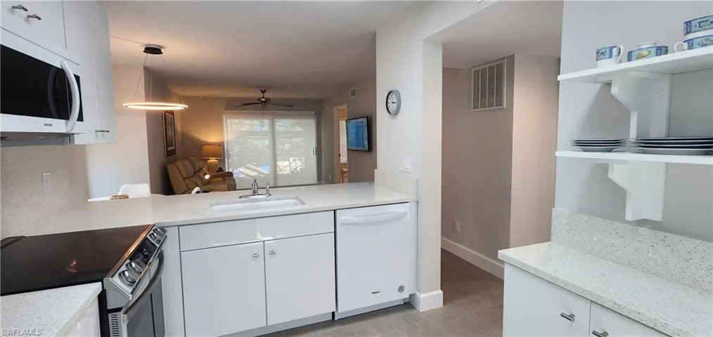 Kitchen with ceiling fan, white appliances, light quartz counters, hanging light fixtures, and sink
