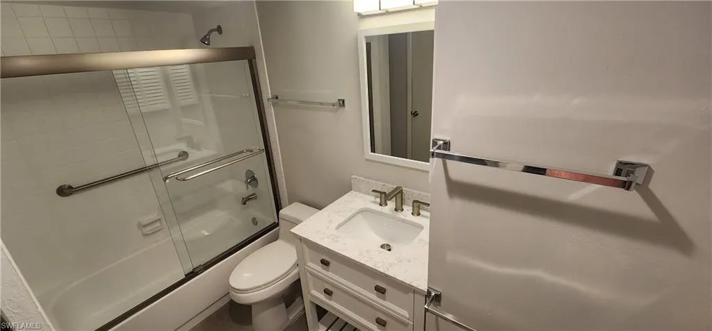 Full bathroom featuring combined bath / shower with glass door, vanity, and toilet
