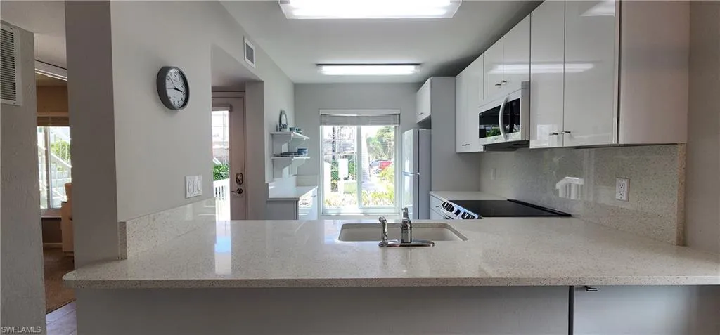 Kitchen with quartz countertops, white refrigerator, backsplash, sink, and white cabinetry