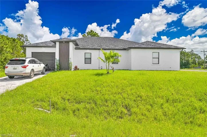 View of front of property with an attached garage, stucco siding, driveway, a front lawn, and roof with shingles