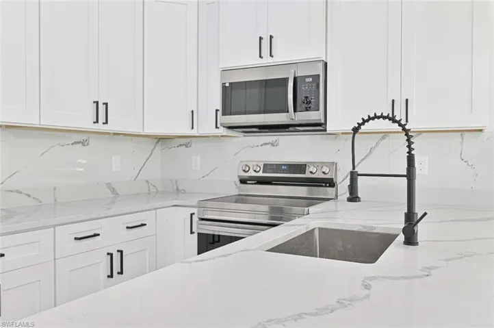 Kitchen with white cabinetry, tasteful backsplash, light stone countertops, and stainless steel appliances