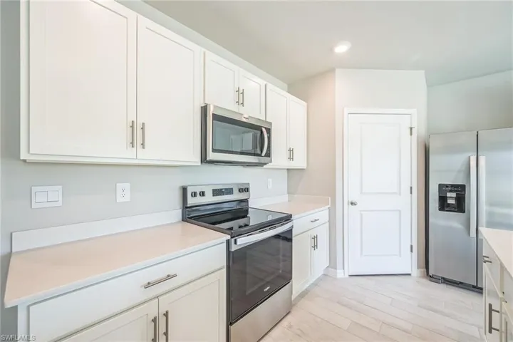 Kitchen with stainless steel appliances, white cabinetry, and light wood-style floors