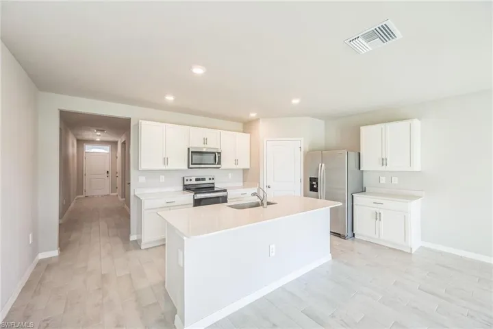 Kitchen with stainless steel appliances, white cabinets, light wood-type flooring, a center island with sink, and recessed lighting