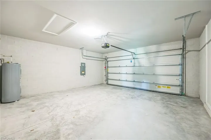 Garage featuring water heater, concrete block wall, electric panel, and a garage door opener