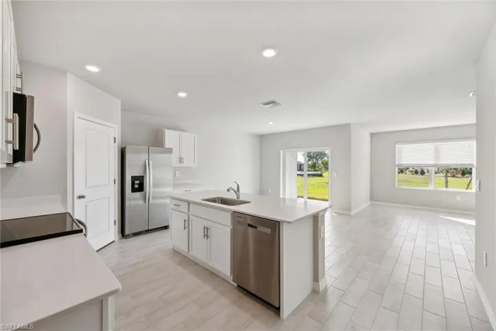 Kitchen with stainless steel appliances, wood finish floors, white cabinetry, an island with sink, and recessed lighting