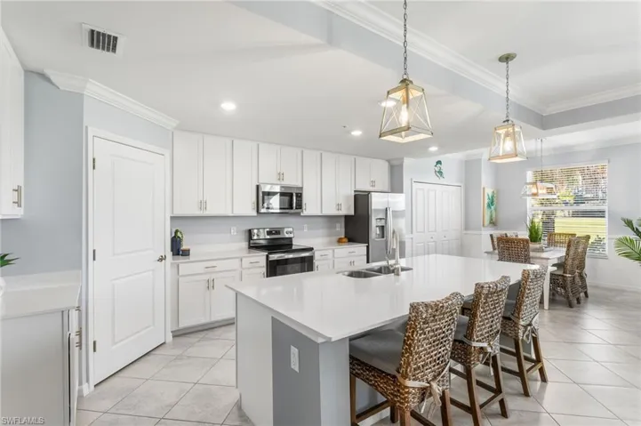 Kitchen featuring ornamental molding, stainless steel appliances, a kitchen bar, white cabinets, and a center island with sink