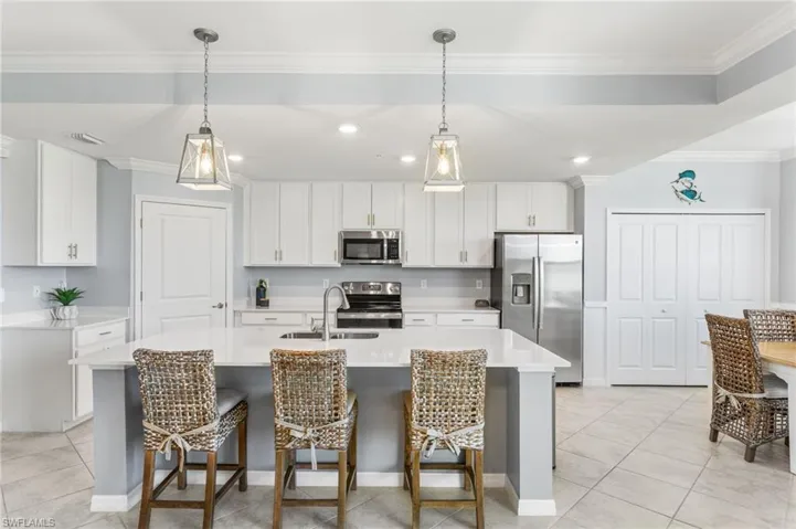 Kitchen with stainless steel appliances, white cabinetry, a kitchen breakfast bar, decorative light fixtures, and crown molding