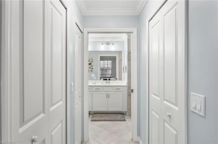 Bathroom with a closet, vanity, crown molding, and light tile patterned flooring