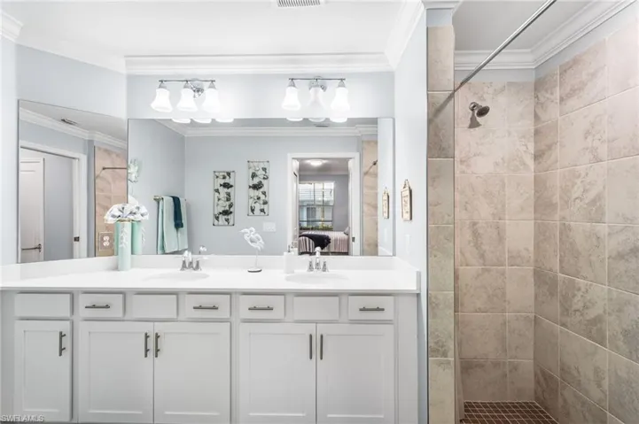 Bathroom with double vanity, connected bathroom, crown molding, and a tile shower