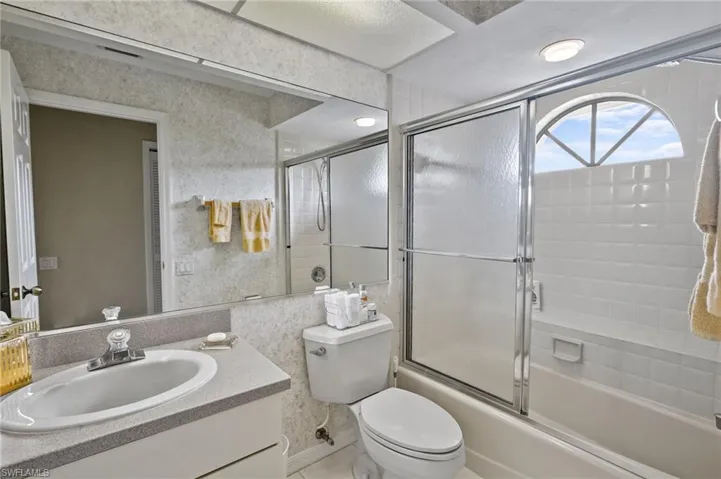 Full bath with vanity, enclosed tub / shower combo, and wallpapered walls