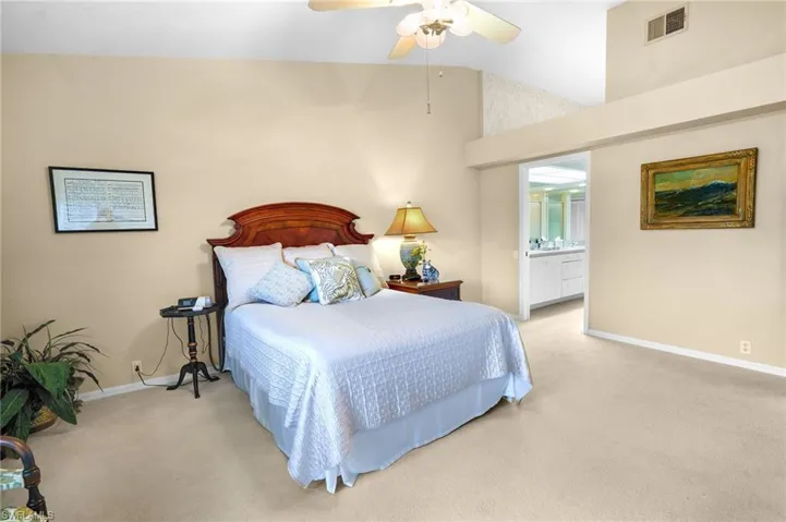 Bedroom with carpet, ensuite bathroom, lofted ceiling, and a ceiling fan