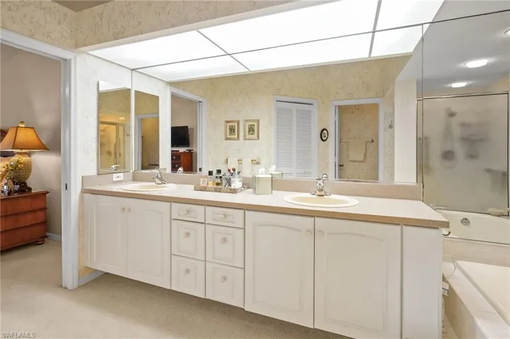 Full bath featuring double vanity, light colored carpet, and tiled shower / bath combo