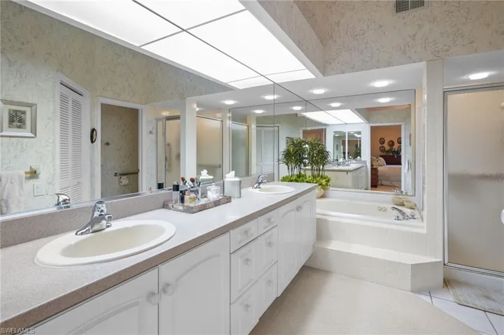 Ensuite bathroom with double vanity, a stall shower, light tile patterned floors, a garden tub, and a closet