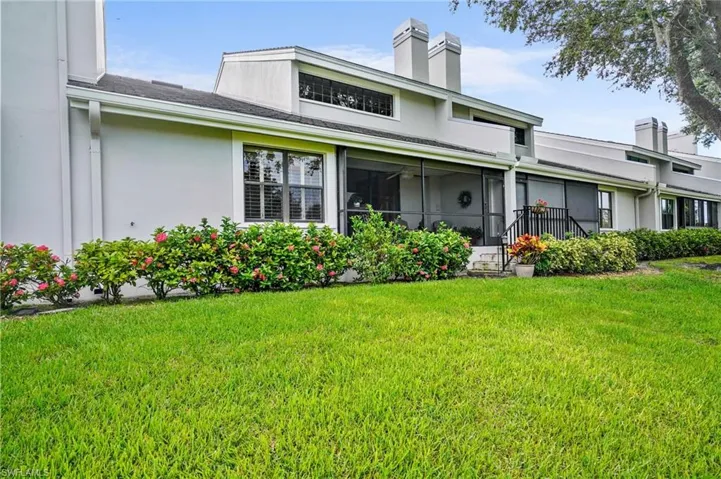 Back of house featuring a yard, a chimney, stucco siding, and a sunroom
